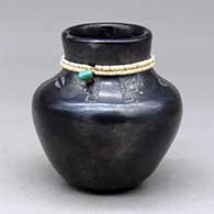 A black jar with a band of heishi beads around the neck with a piece of turquoise, above a band of sgraffito deer tracks and geometric design
 by Kathy Sanchez of San Ildefonso