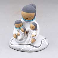 A grandmother storyteller figure wearing a skirt and with three children in her lap
 by Stella Teller of Isleta