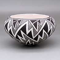 A black-on-white bowl decorated with a lightning bolt and geometric design around the body
 by Carmel Lewis of Acoma