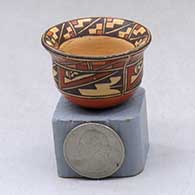 A miniature polychrome bowl with a flared rim and decorated inside the rim with a geometric design and around the body with a four panel geometric design
 by Nathan Begaye of Hopi
