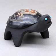 A black turtle figure decorated with sienna spots and a sgraffito hummingbird, flower, butterfly and geometric design, plus inlaid stones
 by Melony Gutierrez of Santa Clara