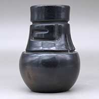 A tall neck black jar decorated with a carved stylized avanyu design around the neck, click or tap to see a larger version