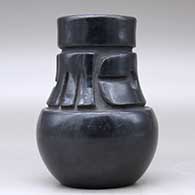 A tall neck black jar decorated with a carved stylized avanyu design around the neck, click or tap to see a larger version