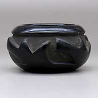 A black bowl carved with a four-panel geometric design around the body, click or tap to see a larger version