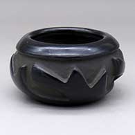 A black bowl carved with a four-panel geometric design around the body
 by Anita Suazo of Santa Clara