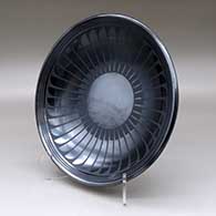 A black on gunmetal black plate decorated with a ring of feathers and geometric design, click or tap to see a larger version