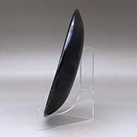 A black on gunmetal black plate decorated with a ring of feathers and geometric design, click or tap to see a larger version