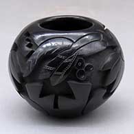 A small black jar decorated around the body with a carved and sgraffito dragonfly, plant, flower and geometric design
 by Autumn Borts of Santa Clara