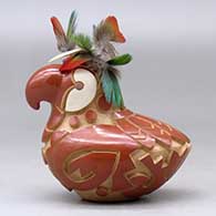 A red and golden micaceous parrot figure decorated with a carved and painted bird element design, plus feathers on the head, click or tap to see a larger version