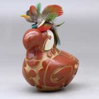 A red and golden micaceous parrot figure decorated with a carved and painted bird element design, plus feathers on the head, click or tap to see a larger version