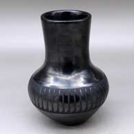 A black on black tall neck jar decorated with a band of feathers around the shoulder
 by Maria Martinez of San Ildefonso