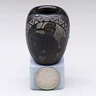 A miniature black cylinder decorated with a sgraffito porcupine, tree branch, sun-face with feathers and geometric design, plus 2 inlaid stones
 by Red Starr of NonPueblo