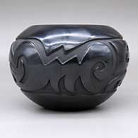 A black bowl carved with a stylized avanyu and geometric design, click or tap to see a larger version