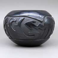 A black bowl carved with a stylized avanyu and geometric design, click or tap to see a larger version