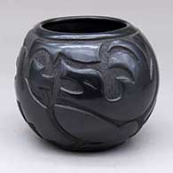A black jar carved with an avanyu, sun face and geometric design
 by Myra Little Snow of Santa Clara