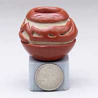 A miniature red jar carved with an avanyu design around and above the shoulder
 by Teresita Naranjo of Santa Clara