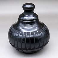 A lidded black-on-black jar decorated with a band of feathers above the shoulder and a geometric design below the shoulder
 by Carmelita Dunlap of San Ildefonso