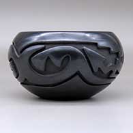 An open black bowl carved around the body with an avanyu and geometric design, click or tap to see a larger version