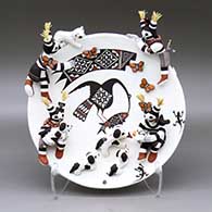 A polychrome plate with a cloudeater, fish, butterflies and a geometric design in the center, surrounded by applique koshare children with a kitten and a canteen, giving water to several puppies
 by Marilyn Ray of Acoma