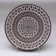 A black-on-white plate decorated with a North Star fine line, pumpkin seed snowflake and geometric design
 by Rebecca Lucario of Acoma