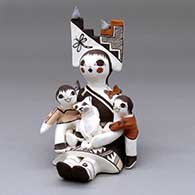 A sitting grandmother storyteller figure wearing a tablito and holding 2 children, a cat, butterfly, birds and a lady bug
 by Judy Lewis of Acoma