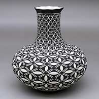 A black on white vase with a pie crust rim and decorated with a pumpkin seed and geometric design
 by Paula Estevan of Acoma