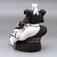 A sitting grandmother storyteller figure holding two children and kittens, butterflies, lady bugs, a bird and a pot, click or tap to see a larger version