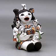 A sitting grandmother storyteller figure holding two children and kittens, butterflies, lady bugs, a bird and a pot, click or tap to see a larger version