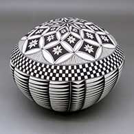 A black on white seed pot decorated with a feather, flower, checkerboard and geometric design
 by Cletus Victorino of Acoma