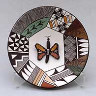A small polychrome plate decorated with a butterfly applique and a fineline and geometric design
 by George Concho Jr of Acoma