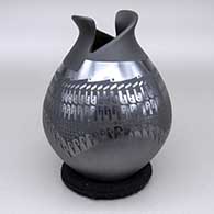 A black on black jar with a geometric cut opening and a sgraffito and painted textured and geometric design
 by Susy Martinez of Mata Ortiz and Casas Grandes
