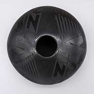A black on black jar with a flat shape and a painted bird and geometric design
 by Octavio Andrew of Mata Ortiz and Casas Grandes