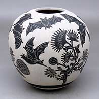 A black-on-white jar decorated with a lightly-carved and sgraffito flying bat design
 by Adrian Corona of Mata Ortiz and Casas Grandes