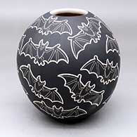 A black-on-white jar decorated with a lightly-carved and sgraffito flying bat design
 by Adrian Corona of Mata Ortiz and Casas Grandes