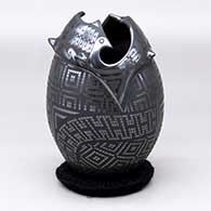 A black on glossy black jar with a geometric cut rim and decorated with a three panel tiny square and geometric design around the body
 by Eligio Ortiz of Mata Ortiz and Casas Grandes