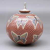 A polychrome jar decorated with a sgraffito and painted butterfly, mesh and geometric design, with a butterfly on the lid, click or tap to see a larger version