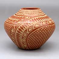 A red jar decorated with a sgraffito snowflake, feather and geometric design
 by Wilma Baca Tosa of Jemez