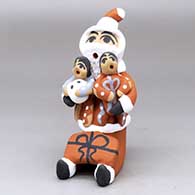 A sitting Santa Claus storyteller figure with two children and a gift
 by Felicia Fragua of Jemez