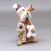 A sitting canine Santa with a Santa hat on one ear and holding a candy cane and a bone
 by Darrick Tsosie of Jemez