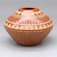 A red jar decorated with a sgraffito snowflake design below the shoulder and a sgraffito feather and geometric design above
 by Wilma Baca Tosa of Jemez