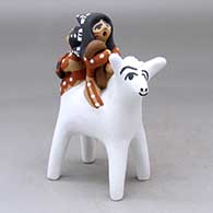 A polychrome figure of two children, one with a headdress, one with a blanket, riding on the back of a white horse
 by Felicia Fragua of Jemez
