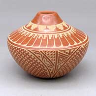 A red jar with a narrow opening and decorated with a sgraffito feather, snowflake and geometric design
 by Wilma Baca Tosa of Jemez