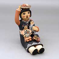 A sitting grandmother storyteller figure holding a basket of corn on her head and with three children in her lap
 by Linda Lucero Fragua of Jemez