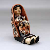 A grandmother storyteller figure wearing a manta and holding three children with gifts, click or tap to see a larger version