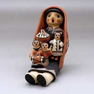 A grandmother storyteller figure wearing a manta and holding three children with gifts
 by Linda Lucero Fragua of Jemez