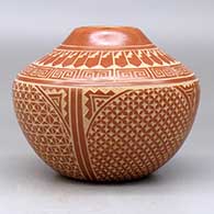 A red jar decorated with a four panel sgraffito spiral, snowflake, feather and geometric design, click or tap to see a larger version