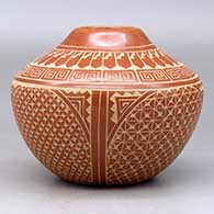 A red jar decorated with a four panel sgraffito spiral, snowflake, feather and geometric design, click or tap to see a larger version