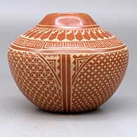 A red jar decorated with a four panel sgraffito spiral, snowflake, feather and geometric design, click or tap to see a larger version