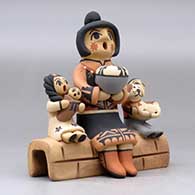 A Singing Mother figure sitting on an adobe wall with three children, a puppy and a pot, click or tap to see a larger version