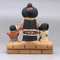 A Singing Mother figure sitting on an adobe wall with three children, a puppy and a pot, click or tap to see a larger version